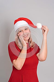 Portrait of a confused blonde 40s woman in a Santa hat on a gray background, vertical photo