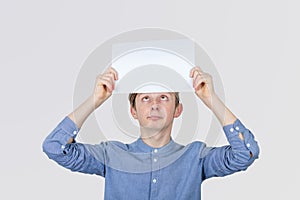 Portrait of confused, thinking young boy seeks a solution looking up, holding a paper over head gray wall background. Human face