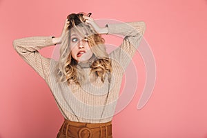 Portrait of confused woman grabbing her head and screaming in puzzlement isolated over pink background