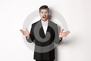 Portrait of confused and worried handsome man in suit, looking at something strange, spread hands sideways and standing