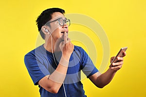 Portrait of confused Young Asian man bitting his finger and listening live music from smartphone with headset