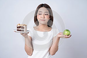 Portrait of a confused young asian woman choosing between cakes and salads