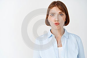 Portrait of confused young woman raising eyebrows and pucker lips puzzled, cant understand, standing in stupor on white
