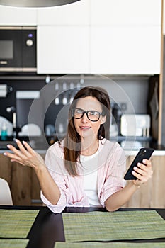 Portrait of confused young woman talking on mobile phone while sitting on a chair at home