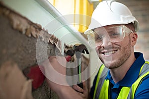 Portrait Of Construction Worker With Chisel Removing Plaster From Wall In Renovated House