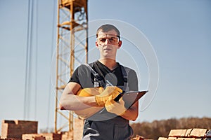 Portrait of construction worker in uniform and safety equipment that stands on rooftop of unfinished building