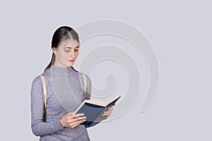 Portrait of contented girl enjoys reading a book, carrying his college backpack on shoulders. Young student girl  ready for exams