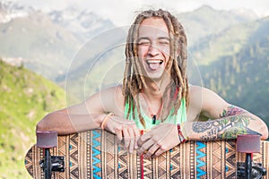 Portrait of cool, funny handsome man with skateboard at mountain