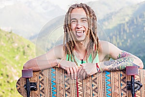 Portrait of cool, funny handsome man with skateboard at mountain