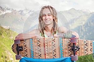 Portrait of cool, funny handsome man with skateboard at mountain