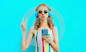 Portrait cool girl blowing red lips sending sweet air kiss holding phone listening to music in wireless headphones on colorful