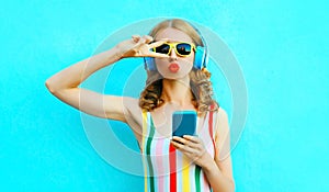 Portrait cool girl blowing red lips sending sweet air kiss holding phone listening to music in wireless headphones on colorful