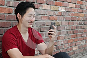 Portrait of a cool guy sitting on sidewalk looking at mobile phone with copy space