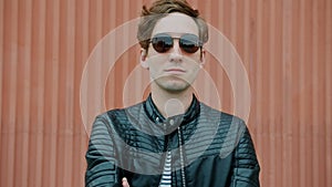 Portrait of cool guy wearing sunglasses and leather jacket standing outdoors with arms crossed