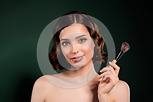 Portrait of cool professional makeup artist girl with naked shoulders hold big brush isolated on green color background