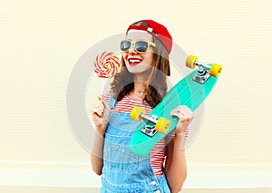 Portrait cool smiling girl with lollipop and skateboard over white