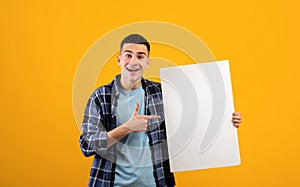 Portrait of cool young guy pointing at empty advertising billboard with mockup for your ad