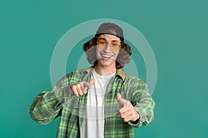 Portrait of cool young guy in sunglasses pointing at you on color background