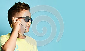 Portrait of a cool young teen guy talking on a mobile phone in summer style clothes in sunglasses, on a blue background.