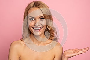 Portrait with copy space of nude, happy smiling girl with big eyes demonstrate empty place on her palm,  on pink