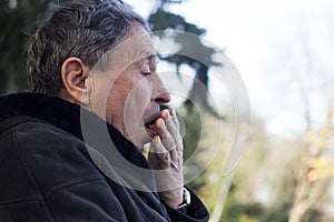 Portrait of a coughing senior man outdoors, looking down