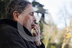 Portrait of a coughing senior man outdoors, looking down