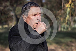 Portrait of a coughing senior man outdoors, looking down