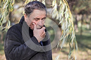 Portrait of a coughing senior man outdoors, looking down