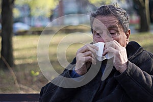 Portrait of a coughing senior man outdoors, looking down