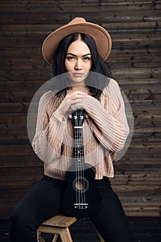 Portrait of country style girl posing with her small guitar on a chair