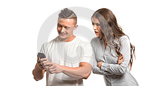 Portrait of couple. Angry upset woman holding arms crossed and looks over husband`s s shoulder at his phone. Man looking