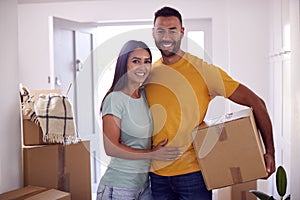 Portrait Of Couple Carrying Boxes Through Front Door Of New Home On Moving Day
