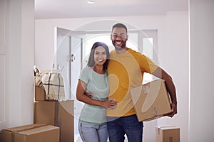 Portrait Of Couple Carrying Boxes Through Front Door Of New Home On Moving Day