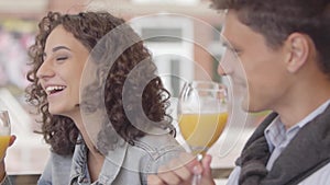 Portrait of couple chatting and laughing while drinking orange juice sitting in cafe outdoors. Young man and woman