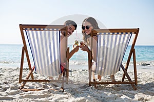 Portrait of couple holding drinks while relaxing on deck chairs at beach