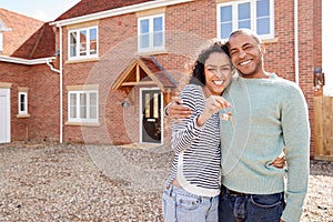 Portrait Of Couple Holding Keys Standing Outside New Home On Moving Day