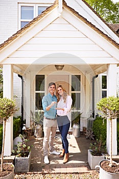 Portrait Of Couple Holding Keys To New Home Standing Outside Front Door