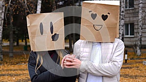 Portrait of couple in love having fun by cover head with paper bags holding hands and looking at camera