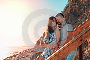 Portrait of a couple of lovers embrace standing on the stairs and pose against the background of the sea and sunset. The concept