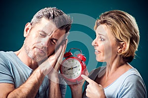 A portrait of couple in the morning. Woman holding alarm clock, while man sleeping. People, relationships and emotions concept