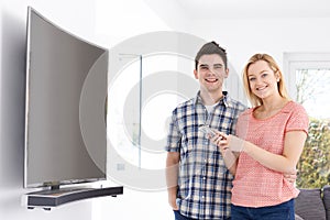 Portrait Of Young Couple With New Curved Screen Television At Ho