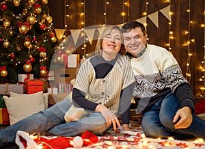 Portrait of a couple in New Year decoration. They pose and have fun. Festive lights, gifts and a Christmas tree decorated with