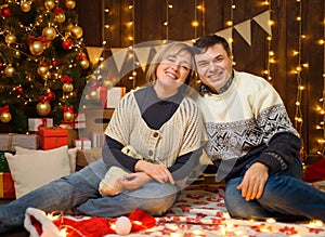 Portrait of a couple in New Year decoration. They pose and have fun. Festive lights, gifts and a Christmas tree decorated with