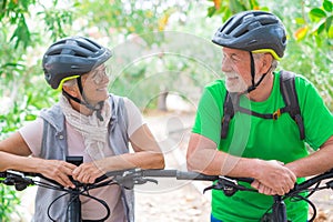 Portrait of couple of old and happy in love seniors looking each other smiling and having fun with their bikes in the nature
