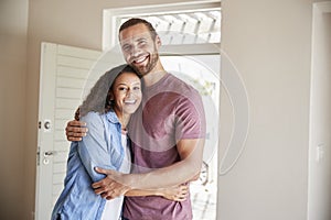 Portrait Of Couple By Open Front Door In Lounge Of New Home
