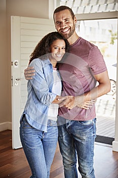 Portrait Of Couple By Open Front Door In Lounge Of New Home