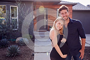 Portrait Of Couple With Pregnant Wife Standing Outdoors In Front Of New Home