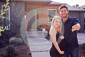 Portrait Of Couple With Pregnant Wife Standing Outdoors In Front Of New Home Holding Keys