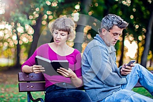 Portrait of couple sitting outside. Woman reading a book, man us