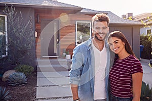 Portrait Of Couple Standing Outdoors In Front Of House With For Sale Sign In Garden photo